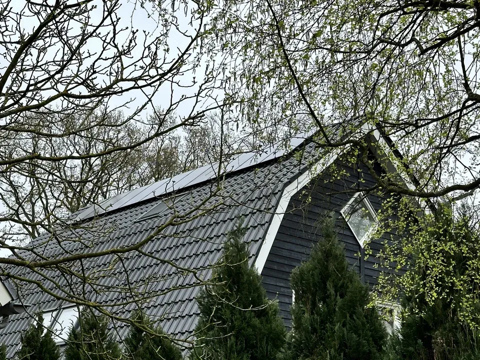 Woning met zonnepanelen op het schuine dak, gezien door de bomen