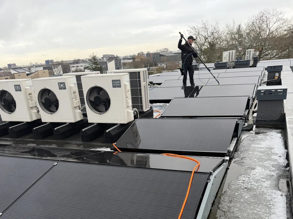 Zonnepanelen reinigen op een bedrijfsdak met een telescoopborstel